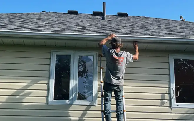 Technician clearing leaves and debris from a residential eavestrough in Collingwood, Ontario
